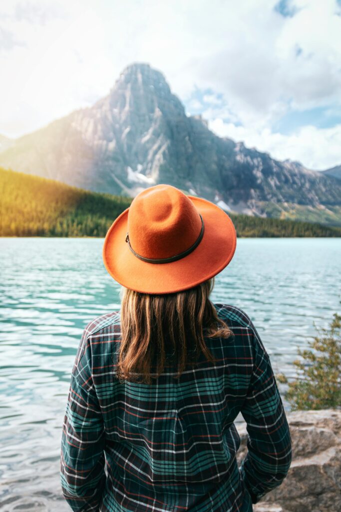 A woman in a fedora enjoys a serene view of a mountain lake in Banff, Canada.