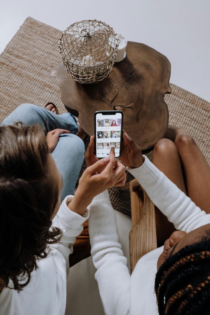 Two people looking at social media on a smartphone at a wooden table.